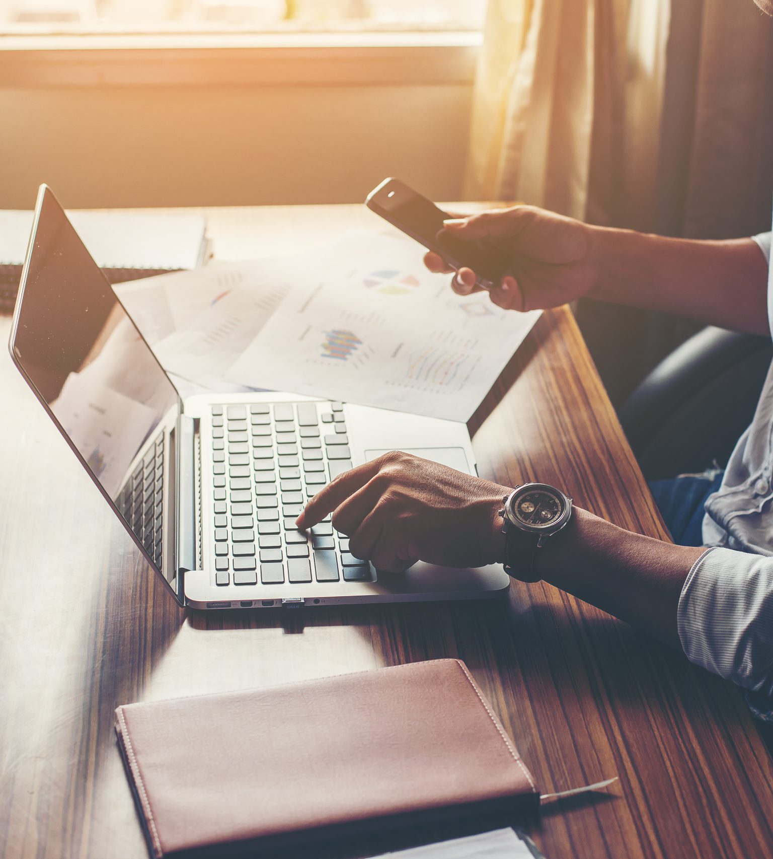 Businessman hands using cell phone with laptop at office desk.